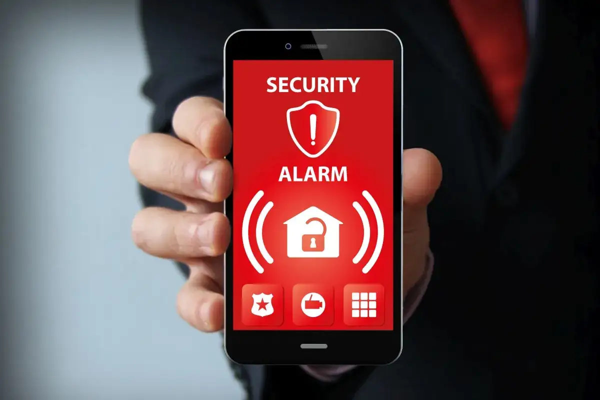 Smartfon z aplikacją alarmową, symbolizującą ochronę przed malware. Czerwony ekran z ikonami bezpieczeństwa.
