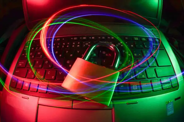 Kłódka na klawiaturze laptopa, otoczona kolorowymi smugami światła, symbolizuje bezpieczeństwo i ochronę danych. Dostępny darmowy antywirus zapewni Ci spokój.