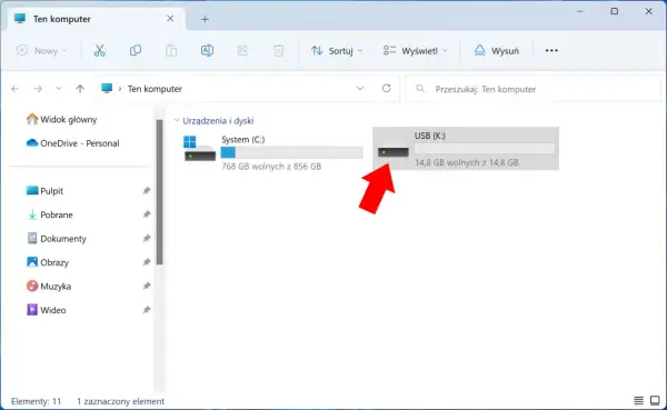 Widok "Ten komputer" z zaznaczonym pendrivem USB (K:). Czerwona strzałka wskazuje na ikonę pendrive'a, sugerując jego szyfrowanie lub przygotowanie do niego.