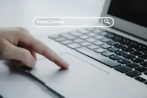 Dłoń na touchpadzie laptopa, pasek adresu z "https://www.", symbol lupy. Bezpieczna poczta online.