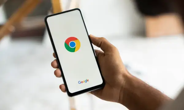 Dłoń trzyma smartfon z logo Chrome. Chcesz wiedzieć, jak usunąć synchronizację Google?