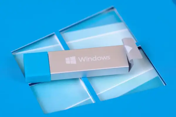 Srebrny pendrive startowy Windows 10 z niebieską nakładką, leżący na niebieskim tle z logo Windows.