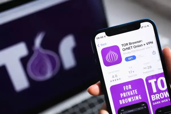 Aplikacja TOR Browser na telefonie, obok logo TOR na ekranie laptopa. Dowiedz się, jak wejść do darknetu, korzystając z tej przeglądarki.